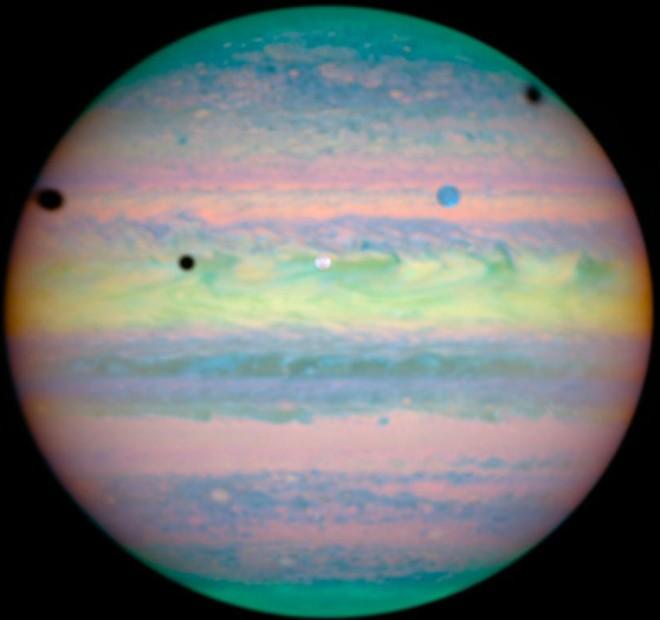 Photographed in Near-infrared Light on March 28, 2004 is a Grand View of Jupiter and a Rare Triple Alignment and Rare Triple Eclipse of Its Three Largest Moons: Io (white circle, center), Ganymede (blue circle, upper right), and Callisto (not shown).  Evidence of This Rare Combination of Celestial Events is Seen by Shadows Cast by the Moons - the Three Black Circles: Io (slightly above center, to the left), Ganymede (left edge), and Callisto (near right edge). Photo Credit: Hubble Spots Rare Triple Eclipse on Jupiter, March 28, 2004 (Release date: November 4, 2004), STScI-2004-30, NASA's Earth-orbiting Hubble Space Telescope; European Space Agency (ESA, http://www.esa.int), Erich Karkoschka (University of Arizona, USA), National Aeronautics and Space Administration (NASA, http://www.nasa.gov), Government of the United States of America (USA).