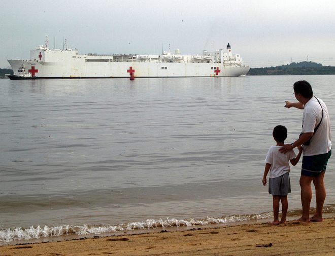 With Gentle Waves Splashing at Their Feet, a Father Shows His Young Son (lower right) the Enormous Military Sealift Command Hospital Ship USNS Mercy (T-AH 19) as it Transits the Johor Strait That Separates Singapore and Malaysia. The USNS Mercy is an important part of Operation Unified Assistance, a massive international humanitarian operation to relieve the extensive suffering caused by the "Great Earthquake and Catastrophic Tsunami of 2004" <http://ChamorroBible.org/gpw/gpw-The-Great-Earthquake-and-Catastrophic-Tsunami-of-2004.htm>. The ship contains 12 fully equipped operating rooms, a 1,000-bed hospital facility, digital radiological services, a diagnostic and clinical laboratory, a pharmacy, an optometry lab, a CAT scan, and 2 oxygen producing plants. January 29, 2005, Republic of SingaporePhoto Credit: Lt. Chuck Bell, Navy NewsStand - Eye on the Fleet Photo Gallery (http://www.news.navy.mil/view_photos.asp, 050129-N-0493B-007), United States Navy (USN, http://www.navy.mil); United States Department of Defense (DoD, http://www.DefenseLink.mil or http://www.dod.gov), Government of the United States of America (USA).