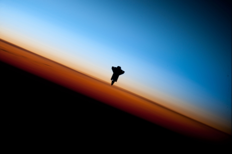 36. Orbital Sunset: Silhouette of Space Shuttle Endeavour (STS-130) and Earth's Colorful Horizon, February 9, 2010, As Seen From the International Space Station (Expedition Twenty-Two) While Orbiting Above the South Pacific Ocean Off the Coast of Southern Chile, South America: Latitude (LAT): -46.9, Longitude (LON): -80.5, Altitude (ALT): 183 Nautical Miles. Photo Credit: STS-130 Shuttle Mission Imagery (http://spaceflight.nasa.gov/gallery/images/shuttle/sts-130/ndxpage1.html), ISS022-E-062673 (http://spaceflight.nasa.gov/gallery/images/shuttle/sts-130/html/iss022e062673.html), NASA Human Space Flight (http://spaceflight.nasa.gov), National Aeronautics and Space Administration (NASA, http://www.nasa.gov), Government of the United States of America. Additional information from NASA: 'The orange layer is the troposphere, where all of the weather and clouds which we typically watch and experience are generated and contained. This orange layer gives way to the whitish Stratosphere and then into the Mesosphere. In some frames the black color is part of a window frame rather than the blackness of space.'