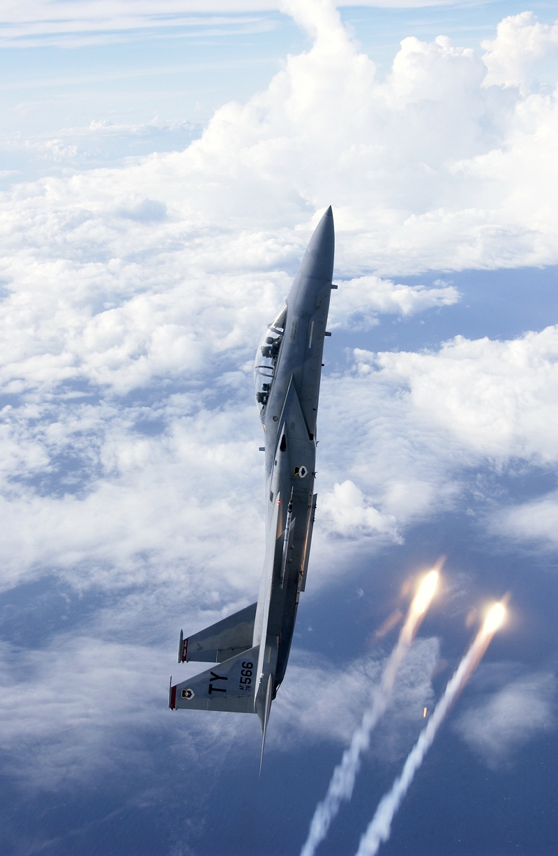 39. A U.S. Air Force F-15D Eagle Fighter Jet In A Vertical Climb Above the Clouds As Flares Streak By. Photo Credit: Staff Sgt. Jeffrey Allen, United States Air Force (USAF, http://www.af.mil, 030814-F-2171A), United States Department of Defense (DoD, http://www.DefenseLink.mil or http://www.dod.gov), Government of the United States of America (USA).
