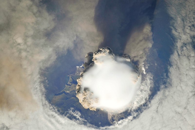 2. Sarychev Peak Volcano Erupts -- Clearing,  Possibly From Its Shock Wave, A Circle In the Cloud Deck Above -- With A Plume of Brown Ash and Steam, June 12, 2009 at 22:15:28 GMT, Matua Island, Kuril Islands, Rossiyskaya Federatsiya -- Russian Federation, As Seen From the International Space Station (Expedition 20) Photo Credit: NASA, International Space Station (Expedition Twenty); ISS020-E-8737, Sarychev Peak, Invisible shock wave, Volcanic plume, Matua Island, Kuril (or Kurile) Islands; Image Science and Analysis Laboratory, NASA-Johnson Space Center. 'Astronaut Photography of Earth - Display Record.' <http://eol.jsc.nasa.gov/scripts/sseop/photo.pl?mission=ISS020&roll=E&frame=8738>; National Aeronautics and Space Administration (NASA, http://www.nasa.gov), Government of the United States of America (USA).