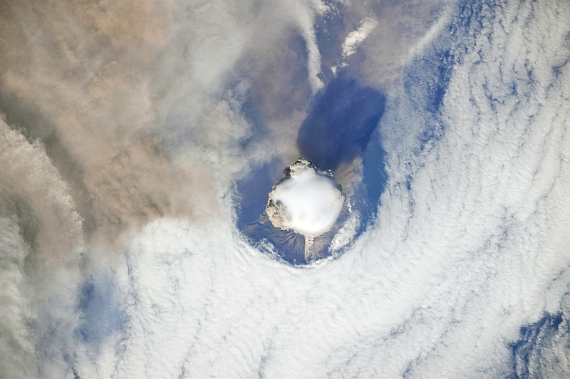 3. Sarychev Peak Volcano Erupts -- Clearing,  Possibly From Its Shock Wave, A Circle In the Cloud Deck Above -- With A Plume of Brown Ash and Steam, June 12, 2009 at 22:15:35 GMT, Matua Island, Kuril Islands, Rossiyskaya Federatsiya -- Russian Federation, As Seen From the International Space Station (Expedition 20) Photo Credit: NASA, International Space Station (Expedition Twenty); ISS020-E-8743, Sarychev Peak, Invisible shock wave, Volcanic plume, Matua Island, Kuril (or Kurile) Islands; Image Science and Analysis Laboratory, NASA-Johnson Space Center. 'Astronaut Photography of Earth - Display Record.' <http://eol.jsc.nasa.gov/scripts/sseop/photo.pl?mission=ISS020&roll=E&frame=8743>; National Aeronautics and Space Administration (NASA, http://www.nasa.gov), Government of the United States of America (USA).