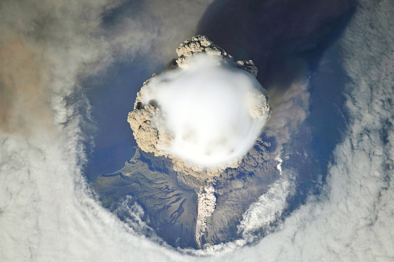 4. Sarychev Peak Volcano Erupts -- Clearing,  Possibly From Its Shock Wave, A Circle In the Cloud Deck Above -- With A Plume of Brown Ash and Steam, June 12, 2009 at 22:15:45 GMT, Matua Island, Kuril Islands, Rossiyskaya Federatsiya -- Russian Federation, As Seen From the International Space Station (Expedition 20) Photo Credit: NASA, International Space Station (Expedition Twenty); ISS020-E-8747, Sarychev Peak, Invisible shock wave, Volcanic plume, Matua Island, Kuril (or Kurile) Islands; Image Science and Analysis Laboratory, NASA-Johnson Space Center. 'Astronaut Photography of Earth - Display Record.' <http://eol.jsc.nasa.gov/scripts/sseop/photo.pl?mission=ISS020&roll=E&frame=8747>; National Aeronautics and Space Administration (NASA, http://www.nasa.gov), Government of the United States of America (USA).