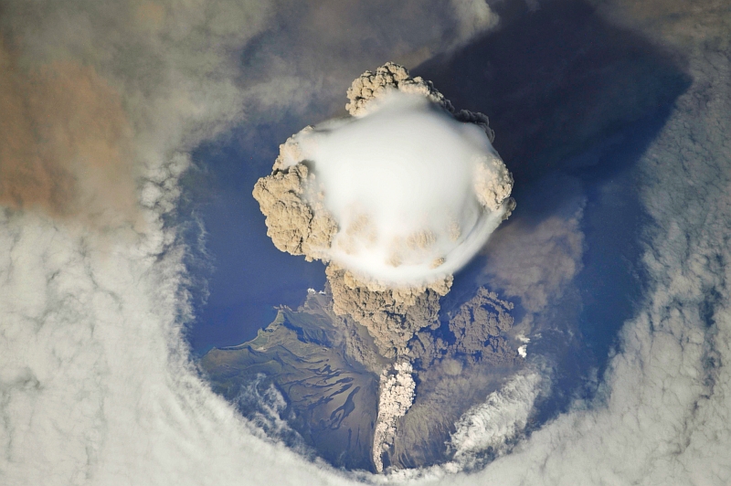 5. Sarychev Peak Volcano Erupts -- Clearing,  Possibly From Its Shock Wave, A Circle In the Cloud Deck Above -- With A Plume of Brown Ash and Steam, June 12, 2009 at 22:15:55 GMT, Matua Island, Kuril Islands, Rossiyskaya Federatsiya -- Russian Federation, As Seen From the International Space Station (Expedition 20) Photo Credit: NASA, International Space Station (Expedition Twenty); ISS020-E-8750, Sarychev Peak, Invisible shock wave, Volcanic plume, Matua Island, Kuril (or Kurile) Islands; Image Science and Analysis Laboratory, NASA-Johnson Space Center. 'Astronaut Photography of Earth - Display Record.' <http://eol.jsc.nasa.gov/scripts/sseop/photo.pl?mission=ISS020&roll=E&frame=8750>; National Aeronautics and Space Administration (NASA, http://www.nasa.gov), Government of the United States of America (USA).