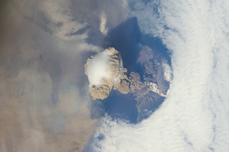 7. Sarychev Peak Volcano Erupts -- Clearing,  Possibly From Its Shock Wave, A Circle In the Cloud Deck Above -- With A Plume of Brown Ash and Steam, June 12, 2009 at 22:16:21 GMT, Matua Island, Kuril Islands, Rossiyskaya Federatsiya -- Russian Federation, As Seen From the International Space Station (Expedition 20) Photo Credit: NASA, International Space Station (Expedition Twenty); ISS020-E-9052, Sarychev Peak, Invisible shock wave, Volcanic plume, Ash cloud, Matua Island, Kuril (or Kurile) Islands; Image Science and Analysis Laboratory, NASA-Johnson Space Center. 'Astronaut Photography of Earth - Display Record.' <http://eol.jsc.nasa.gov/scripts/sseop/photo.pl?mission=ISS020&roll=E&frame=9052>; National Aeronautics and Space Administration (NASA, http://www.nasa.gov), Government of the United States of America (USA).