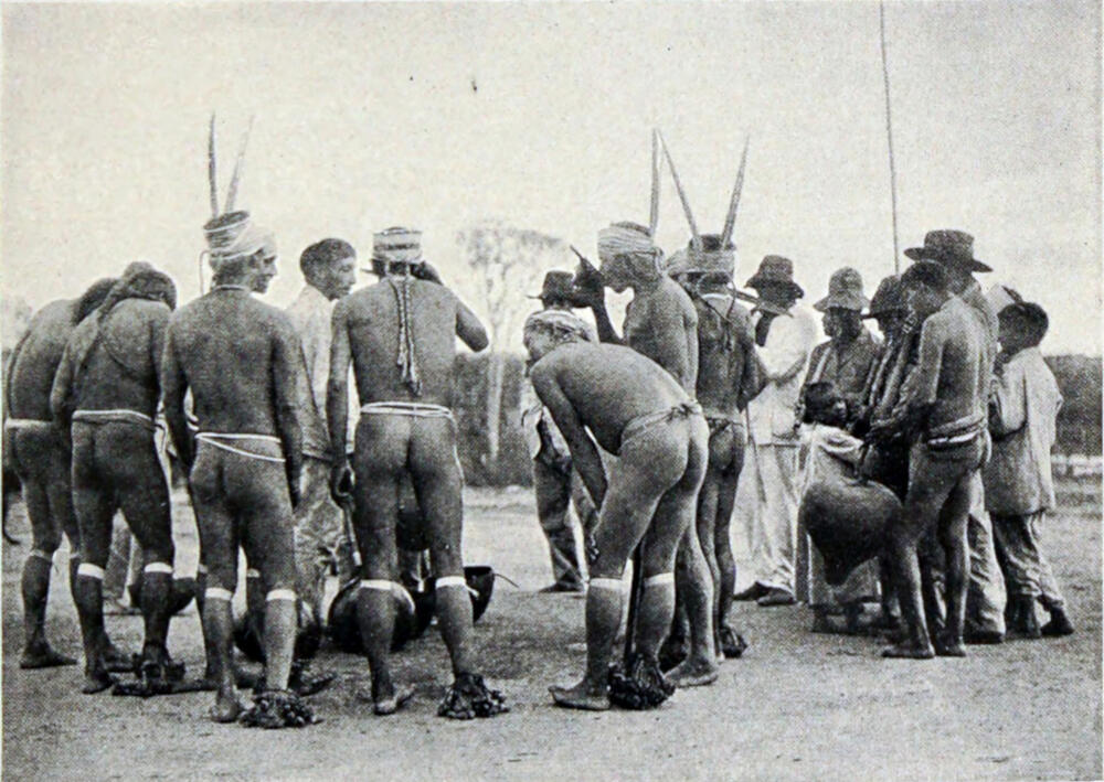 A photograph of a dozen or so men, wearing loincloths, dancing in a circle.