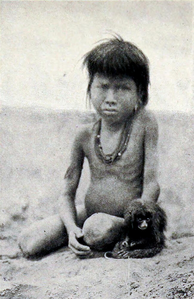 A photograph of a naked native child, sitting on the ground, with a small monkey beside him.
