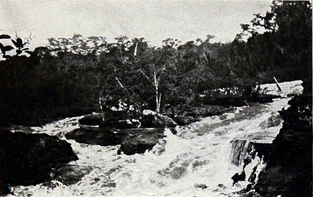 A photograph of a river with rocky banks on either side. The water is rushing toward the camera, very turbulent.