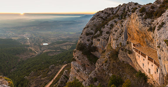 Sunset view of the Ermita de la Virgen de la Peña (Hermitage of the Virgen of the Rock) with the village of Aniés in the front, province of Huesca, Spain. The oldest parts of the sanctuary are romanic and date from the middle edge (13th century). The hermitage is only accesible on foot through a steep path in the forest or caved in the mountain.