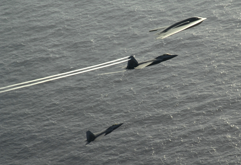 5. The B-2 Spirit and the Two F-22A Raptor Fighter Jets -- the Center Aircraft, An F-22A Raptor, With Trailing Vortices -- Flying In Formation Over the Pacific Ocean, April 7, 2009, Territory of Guam, USA. Photo Credit: Master Sgt. Kevin J. Gruenwald, United States Air Force; Defense Visual Information (DVI, http://www.DefenseImagery.mil, 090414-F-6911G-005) and United States Air Force (USAF, http://www.af.mil), United States Department of Defense (DoD, http://www.DefenseLink.mil or http://www.dod.gov), Government of the United States of America (USA).