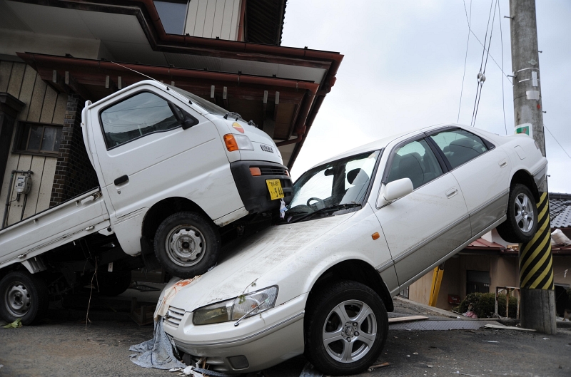 3. A Car Sandwiched Between A Pickup Truck and A Light Pole in Downtown Ofunato, March 15, 2011, Nippon-koku (Nihon-koku) - Japan. Photo Credit: Mass Communication Specialist 1st Class Matthew M. Bradley, United States Navy; Defense Visual Information (DVI, http://www.DefenseImagery.mil, 110315-N-KK192-126) and United States Navy (USN, http://www.navy.mil, 110315-N-2653B-126, http://www.flickr.com/photos/compacflt/5529335693, http://www.flickr.com/photos/compacflt/5529335693/sizes/o/, http://live.staticflickr.com/5258/5529335693_396990ee77_o.jpg), United States Department of Defense (DoD, http://www.DefenseLink.mil or http://www.dod.gov), Government of the United States of America (USA).